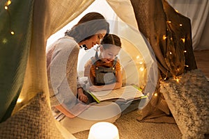 Happy family reading book in kids tent at home