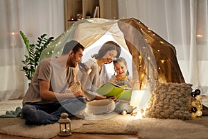 Happy family reading book in kids tent at home