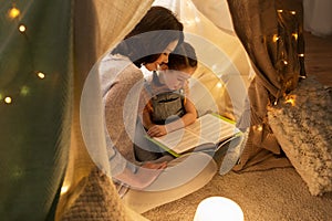 Happy family reading book in kids tent at home