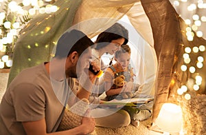 Happy family reading book in kids tent at home