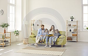 Happy family reading a book while sitting together on a couch in a modern living room