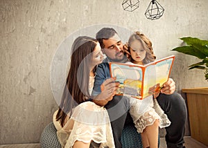 Happy family reading a book to her daughter. Mothers Day.