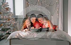 A happy family in red Christmas pajamas reading a book lying in a cozy bed in the morning. new year