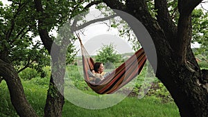 Happy family relaxing in hammock at sunny day in park. Modern mother relaxing and enjoying quality time with her son outside in ha