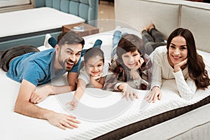 Happy family is relaxing on mattress in orthopedic furniture store. Big family check softness of mattress