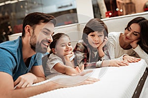 Happy family is relaxing on mattress in orthopedic furniture store. Big family check softness of mattress