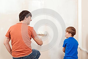 Happy family renovating their new home. Father showing his son how painting wall with a roller