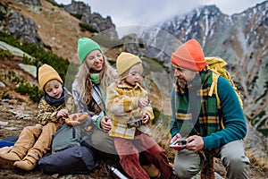 Šťastná rodina odpočívá, svačinu během společné turistiky v podzimních horách.