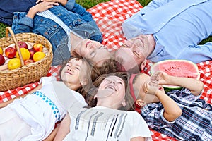 Happy family resting on picnic. Enjoying and lying on checkered plaid in meadow. Adults and children look at the sky