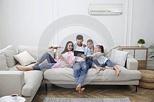 Happy family resting under air conditioner on white wall at home