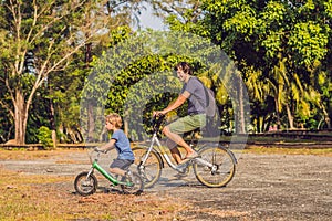 Happy family is riding bikes outdoors and smiling. Father on a bike and son on a balancebike
