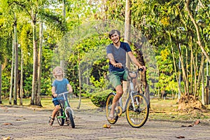 Happy family is riding bikes outdoors and smiling. Father on a bike and son on a balancebike