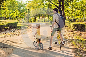 Happy family is riding bikes outdoors and smiling. Father on a bike and son on a balancebike