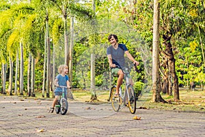 Happy family is riding bikes outdoors and smiling. Father on a bike and son on a balancebike