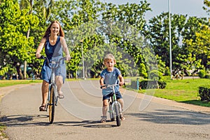 Happy family is riding bikes outdoors and smiling. Mom on a bike and son on a balancebike