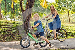 Happy family is riding bikes outdoors and smiling. Mom on a bike and son on a balancebike