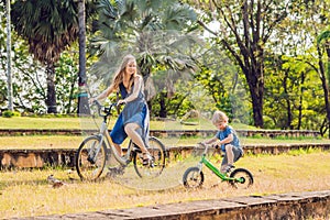 Happy family is riding bikes outdoors and smiling. Mom on a bike and son on a balancebike