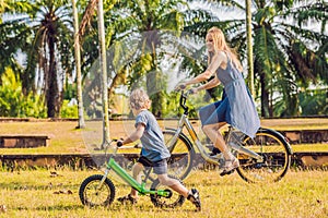 Happy family is riding bikes outdoors and smiling. Mom on a bike and son on a balancebike