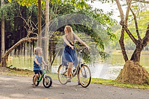 Happy family is riding bikes outdoors and smiling. Mom on a bike and son on a balancebike