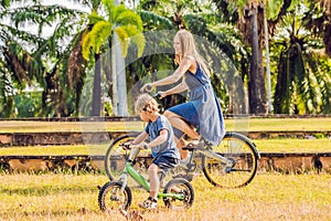 Happy family is riding bikes outdoors and smiling. Mom on a bike and son on a balancebike