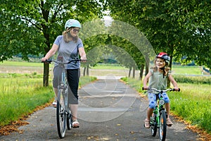 Happy family is riding bikes outdoors and smiling. Mother and daughter, cute little preeschool girl on bicycles, active