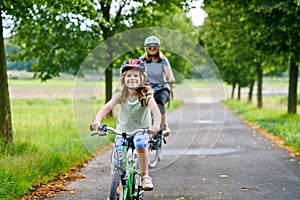 Happy family is riding bikes outdoors and smiling. Mother and daughter, cute little preeschool girl on bicycles, active leisure