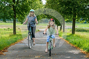 Happy family is riding bikes outdoors and smiling. Mother and daughter, cute little preeschool girl on bicycles, active leisure