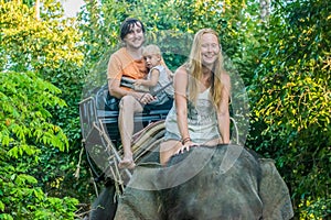 Happy family riding on an elephant, woman sitting on the elephant`s neck