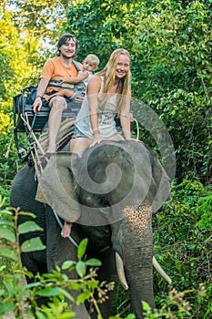 Happy family riding on an elephant, woman sitting on the elephant`s neck