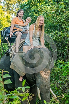 Happy family riding on an elephant, woman sitting on the elephant`s neck