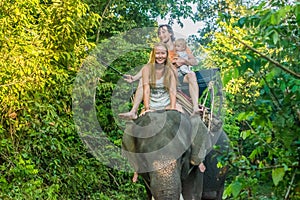 Happy family riding on an elephant, woman sitting on the elephant`s neck