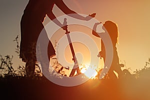 Happy family riding scooter and bike at sunset