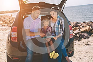 Happy family on a road trip in their car. Dad, mom and daughter are traveling by the sea or the ocean or the river