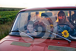 Happy family on a road trip in their car, young mother driving a red retro car with her teen children, enjoying