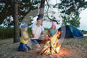 Happy family roasting sausages over campfire. camping and tourism concept