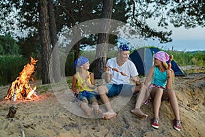 Happy family roasting sausages over campfire. camping and tourism concept