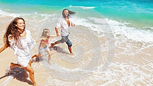 Happy family run together along sea surf on tropical beach