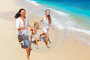 Happy family run together along sea surf on tropical beach