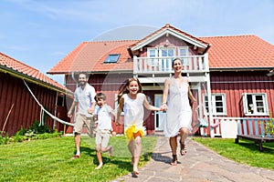 Happy family running on meadow in front of house