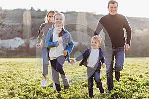 Father, mother and children run through a green field.