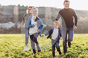 Happy family runs across the field. Father, mother and children run through a green field.