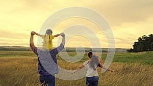 Happy family runs in park holding hands in summer at sunset. Family celebration. Mom, dad and daughter play on field