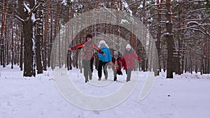 Happy family runs through snowy pine park and laugh. Children play with their parents in winter forest and smile