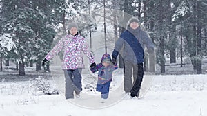 Happy family runs to the camera on a snowy winter day during a snowfall. Mom, dad and child are playing outside.