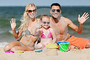 Happy family with sand toys waving hands on beach