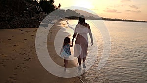 Happy family on sea beach at resort. Mother and daughter playing on the beach at the sunset time. Tropical summer