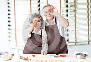 Happy family senior couple holds mold for cookies on eyes place making eyewear having fun in the kitchen at home.Happy family and