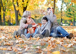 Happy family sit in autumn city park on fallen leaves. Children and parents posing, smiling, playing and having fun. Bright yellow