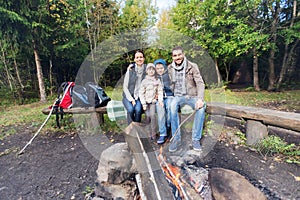 Happy family sitting on bench at camp fire