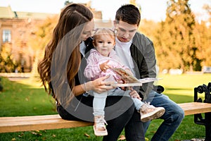 Happy family sitting on the bench in the park with a baby on the mother knees